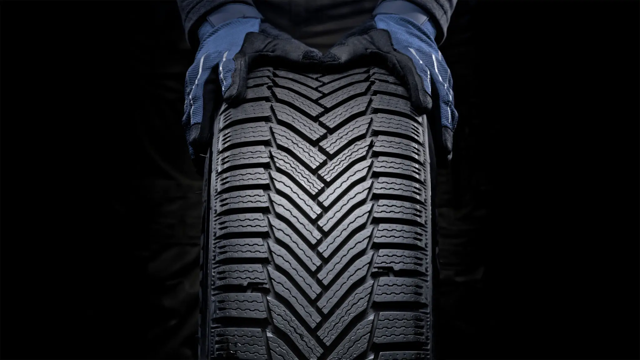 Close-up of a winter tire tread held by gloved hands.